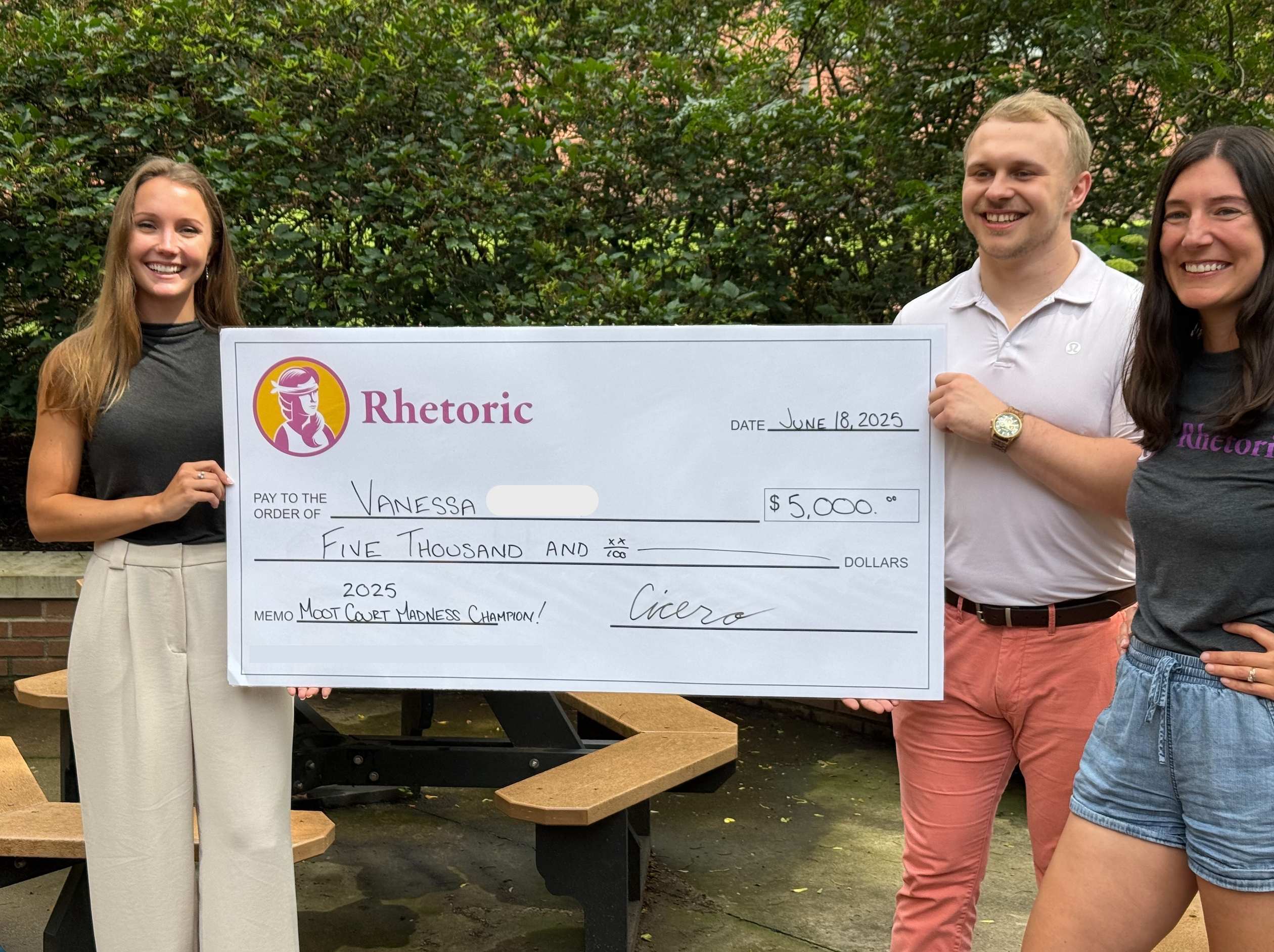 2025 Moot Court Madness champion Vanessa holding a $5,000 prize check with the Rhetoric team